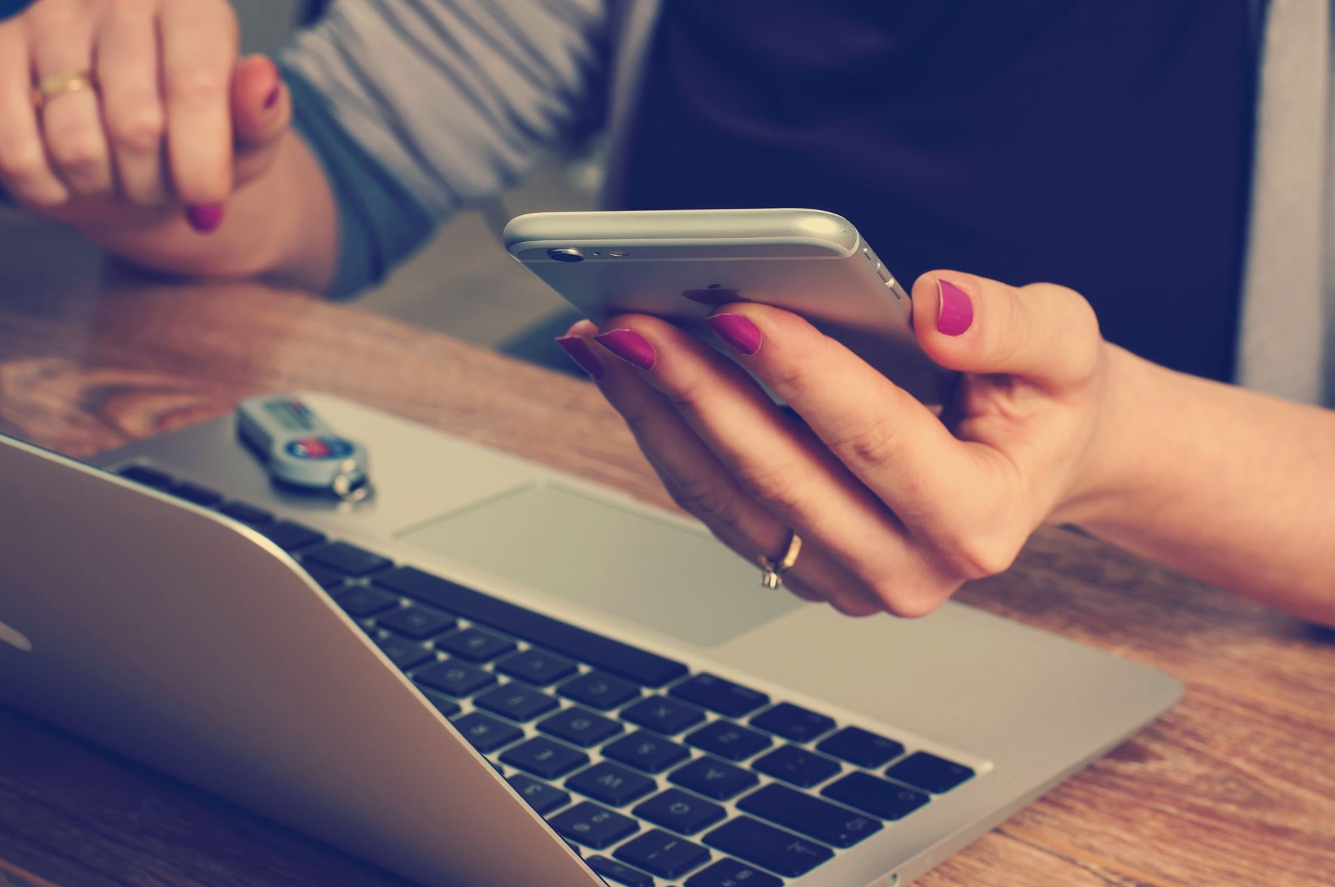 a woman holding a mobile phone, a laptop on the desk in front