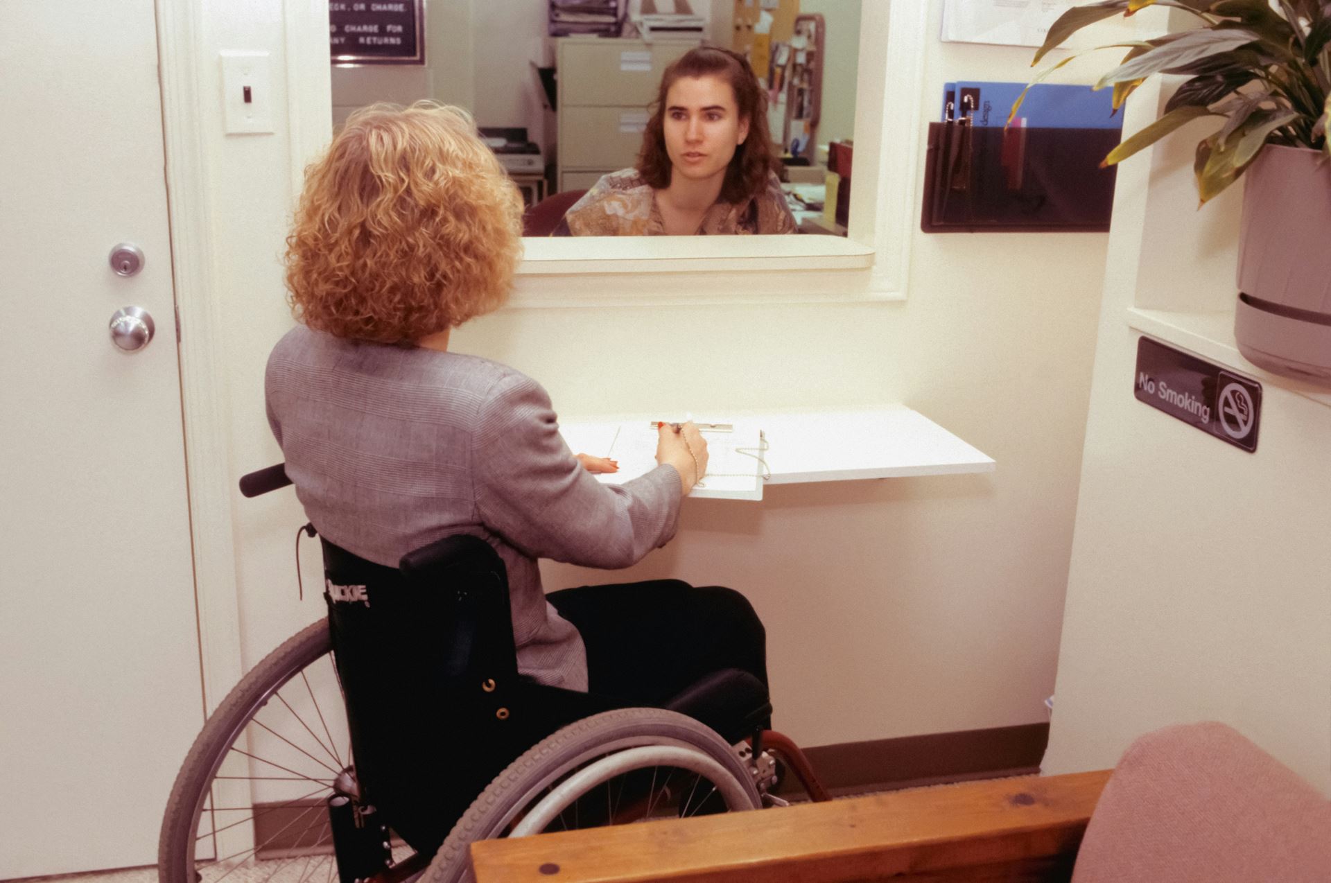 a woman in a wheelchair speaking with a GP Receptionist at a doctor's surgery